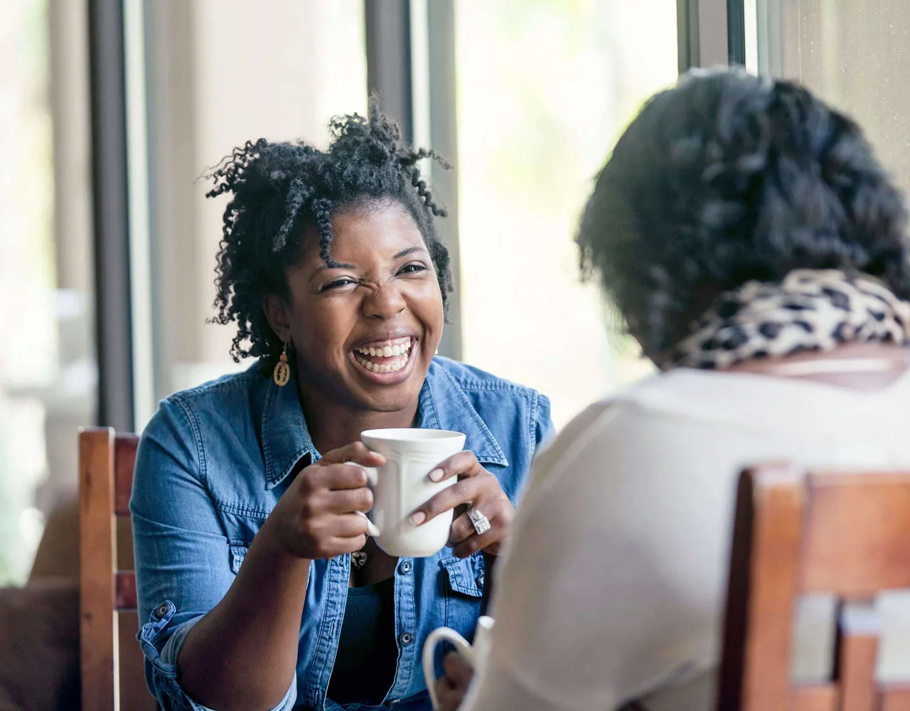 Women laughing hold a coffee cup while chatting with another woman