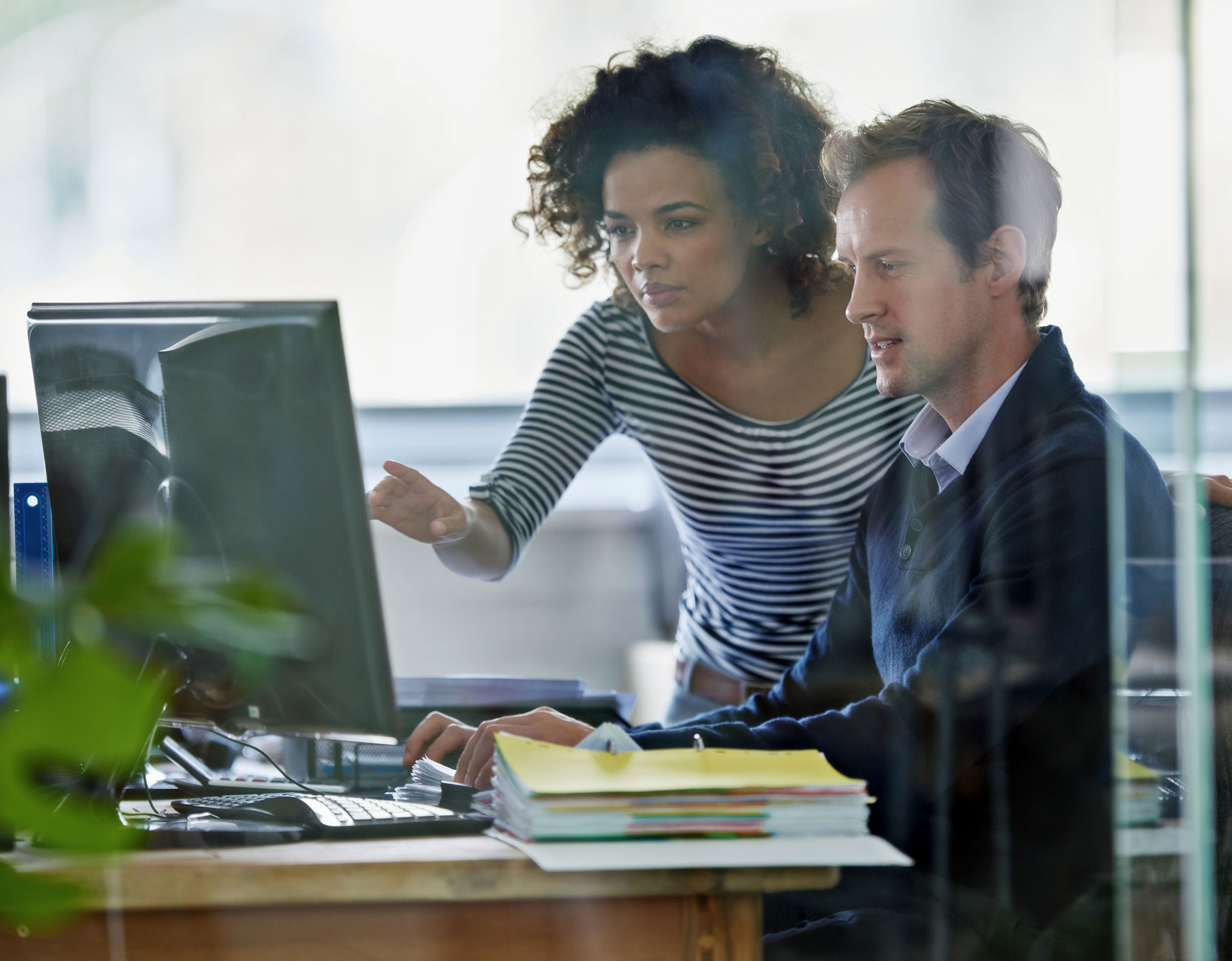 Man At Computer With Female Colleague looking at computer screen