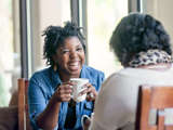 Women laughing hold a coffee cup while chatting with another woman