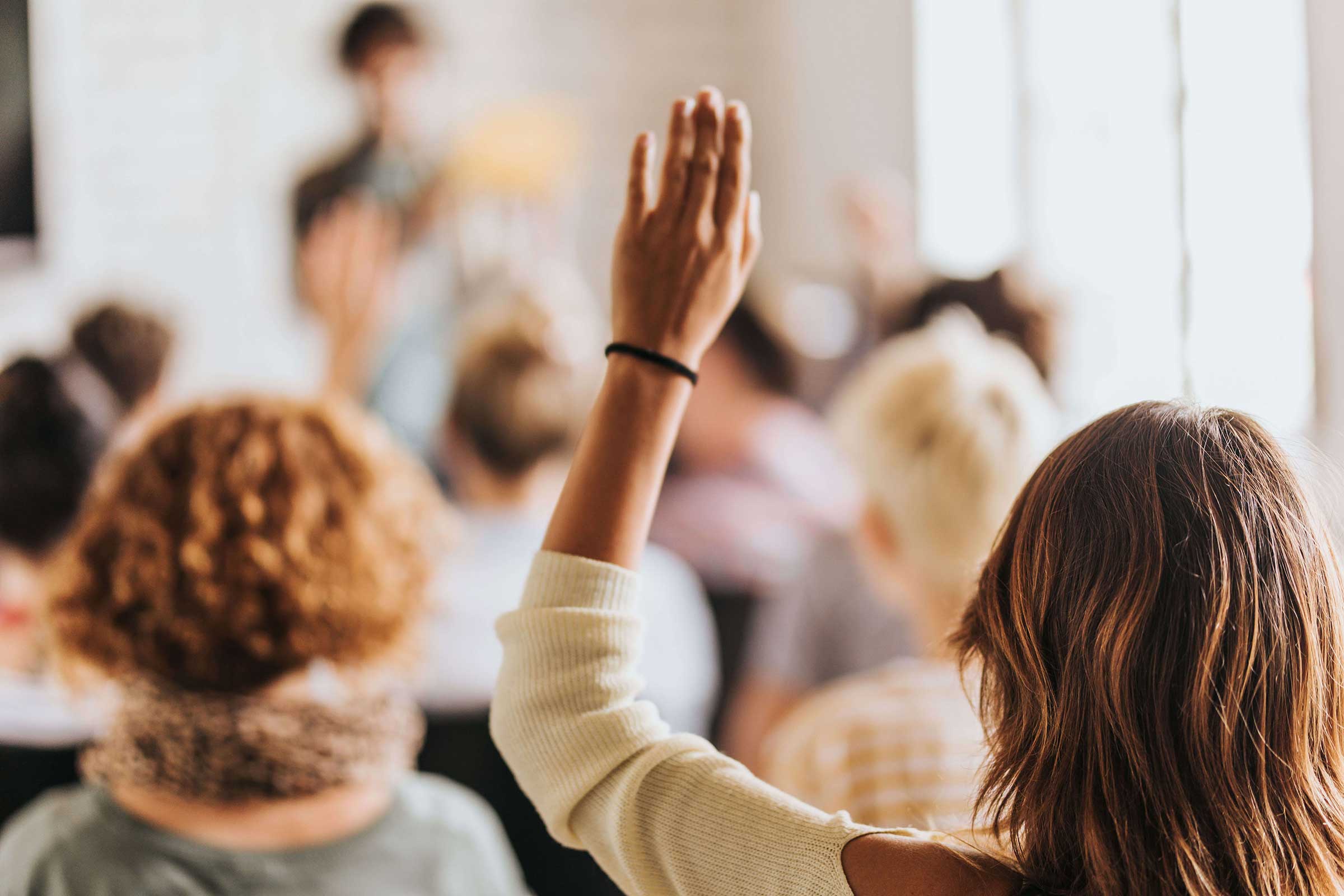 The back of a woman holding her hand up at a talk