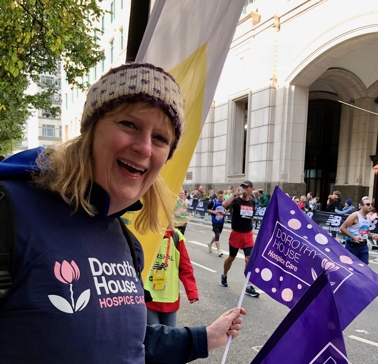 Volunteer in Dorothy House jumper waving flag to support runners